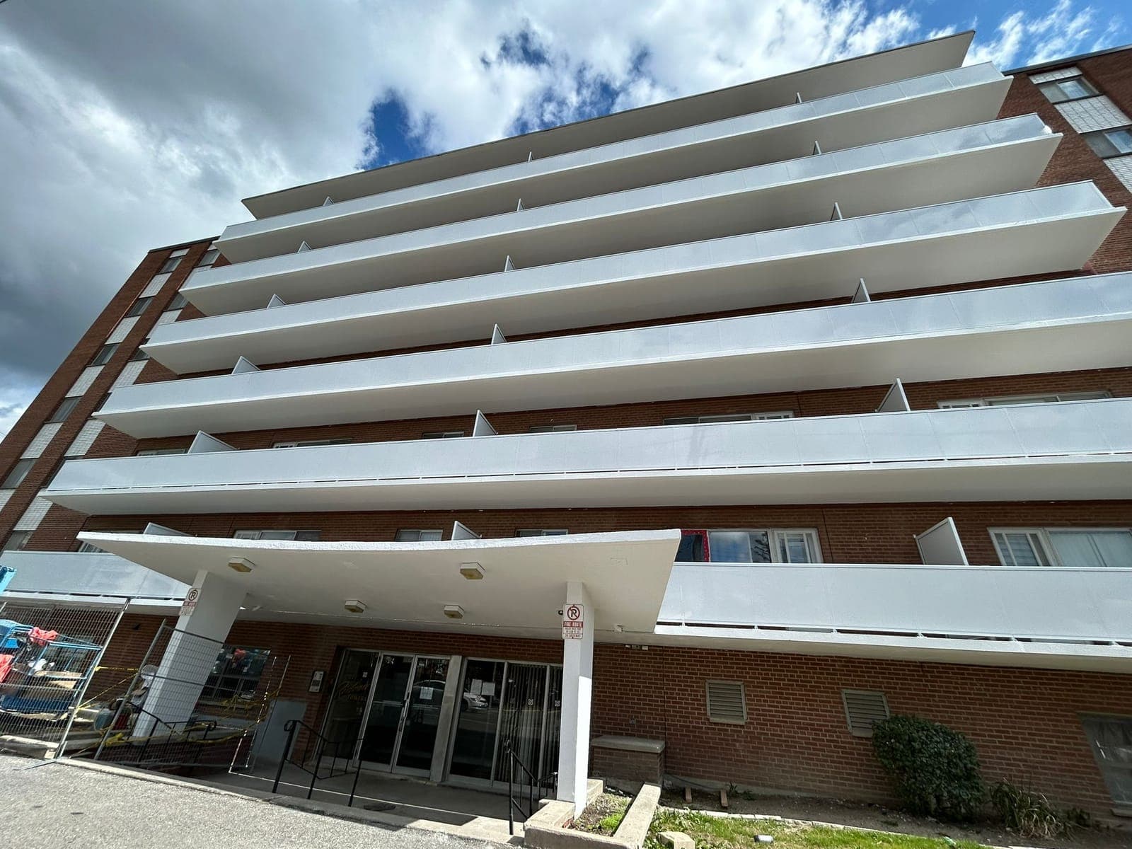 A red-brick apartment building with long white balconies above a canopied entrance