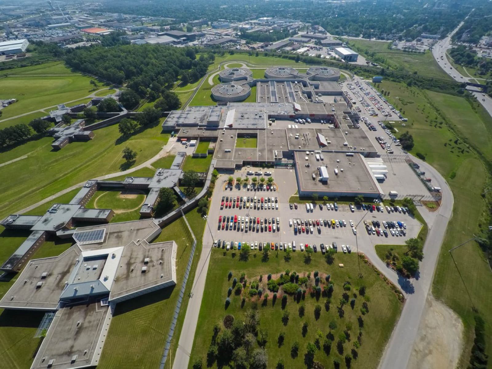 An aerial view of a large institutional complex with parking lots and lawns