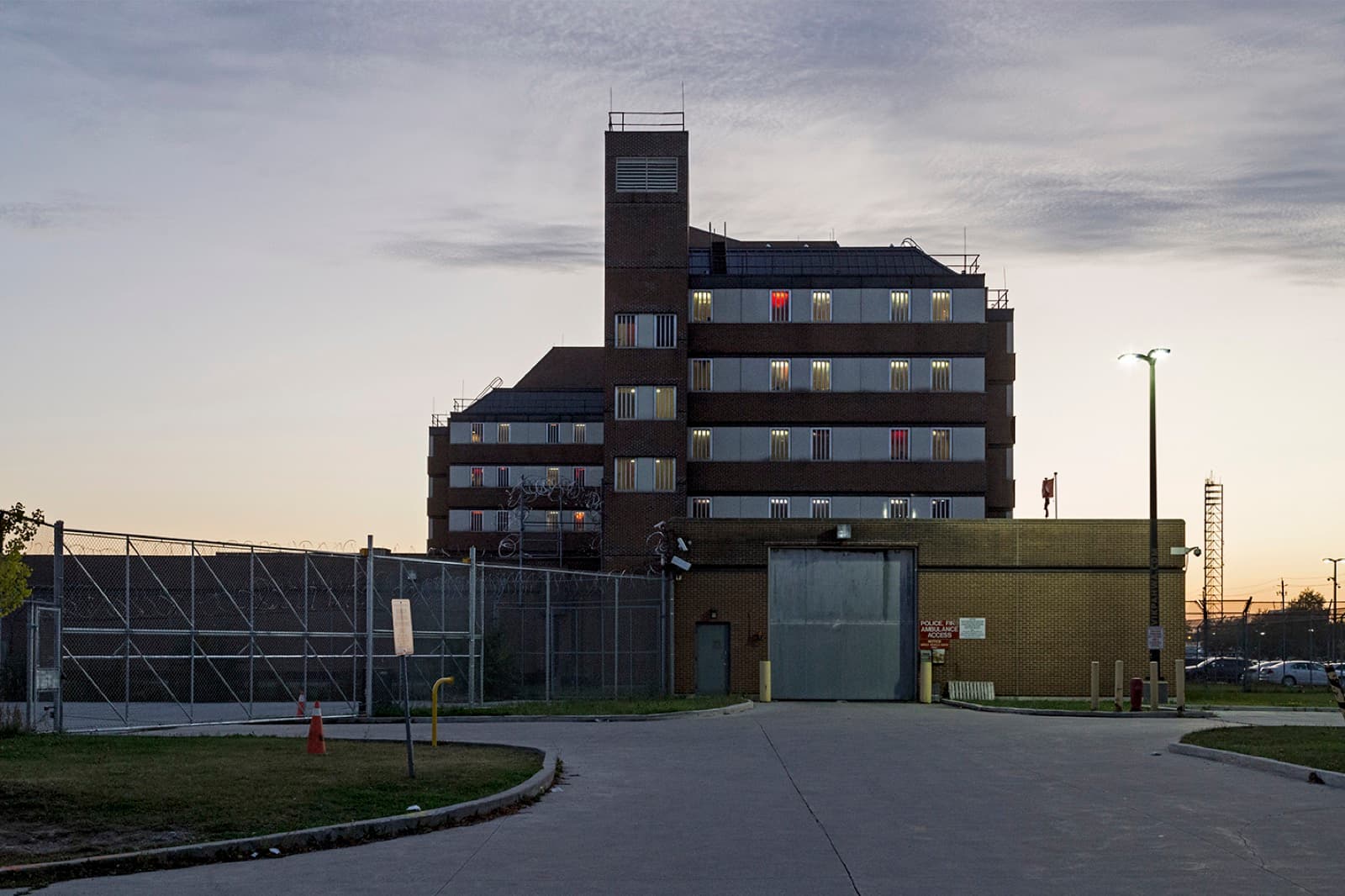 A brick institutional building at dusk behind a fenced entrance road