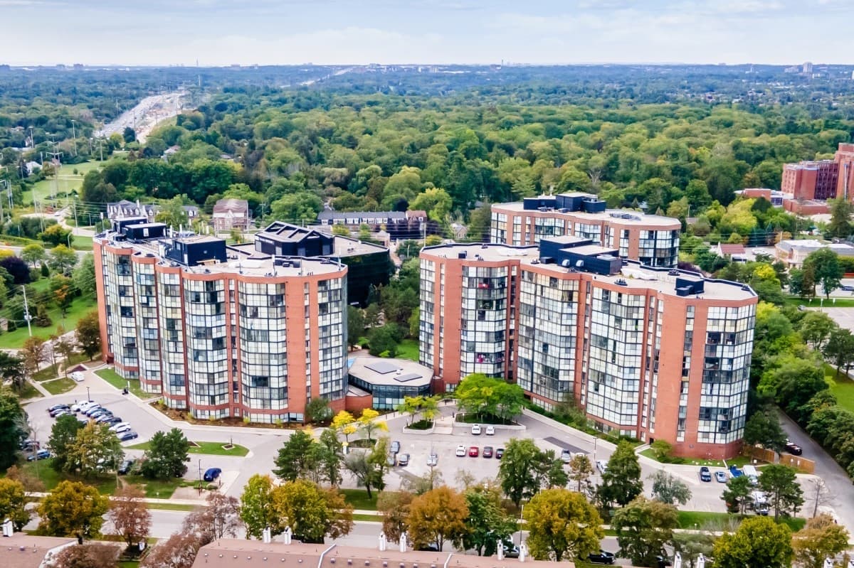An aerial view of two high-rise towers with glass facades among trees and parking areas