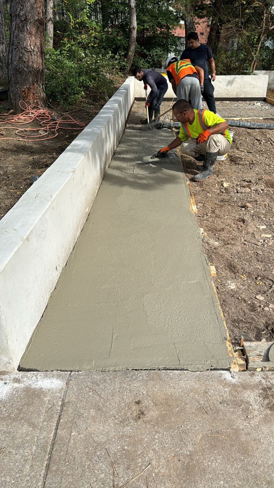 Workers finishing a freshly poured concrete sidewalk beside a new retaining wall