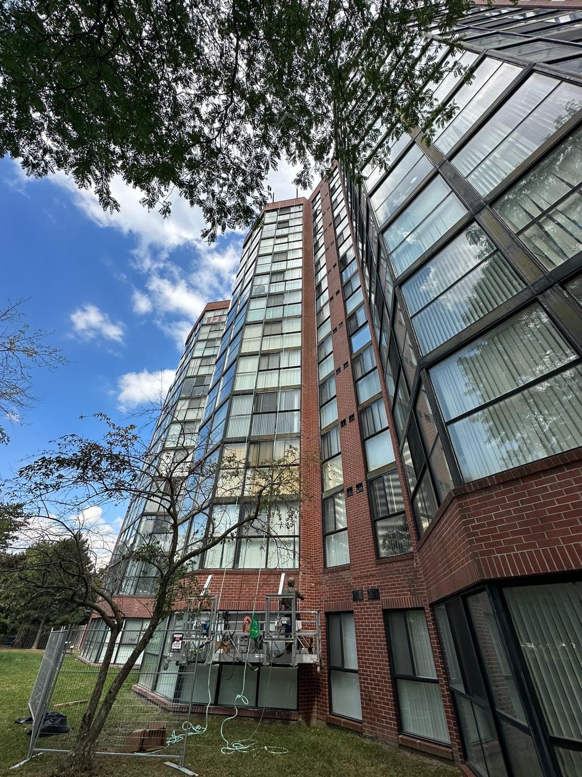 A high-rise residential tower with brick and glass facades, a suspended work platform at its base
